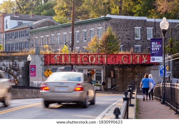 Ellicott City, MD, USA 10/07/2020: Welcome to\
Ellicott City sign written in large capital letters on side of the\
B&O railroad bridge at the entrance of city. Old houses and\
cars passing by are\
seen.