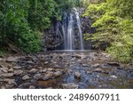 Ellinjaa Falls waterfall long exposure with surrounding rainforest and scattered small rocks in the river beyond the plunge pool near Millaa Millaa on the Atherton Tablelands in Queensland, Australia.