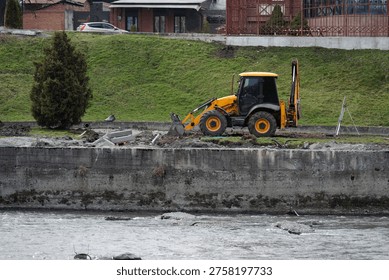 ellow backhoe loader working on a river bank reinforcement project. Construction machinery operating near the water.