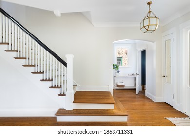 ELMHURST, IL, USA - AUGUST 5, 2020: A renovated stairway in the home's foyer with a view of a mud room and doorway to a small, blue bathroom. A modern light hangs above the hardwood floors.