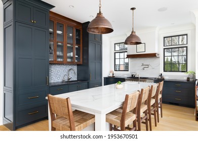 ELMHURST, IL, USA - FEBRUARY 24, 2021: A Luxurious Kitchen With Blue Cabinets, Bronze Dome Light Fixtures Hanging Above The Large White Island, Luxury Appliances, And A Blue Tiled Backsplash.