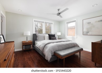 ELMHURST, IL, USA - JANUARY 12, 2021: A cozy bedroom with dark hardwood floors, grey and white bedding, lamps on nightstands, and furniture.