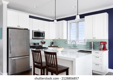 ELMHURST, IL, USA - JANUARY 4, 2022: A Kitchen With White Cabinets And Island, Waterfall Granite Countertop, Blue Walls, And A Green Subway Tile Backsplash.