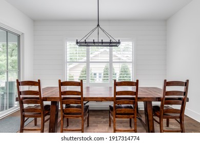 ELMHURST, IL, USA - JULY 10, 2020: A Modern Farmhouse Dining Room With A Shiplap Wall, A Large Wooden Table With Chairs And Bench Seating, And A Large Black Chandelier Hanging From Above.