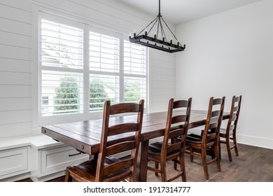 ELMHURST, IL, USA - JULY 10, 2020: A Modern Farmhouse Dining Room With A Shiplap Wall, A Large Wooden Table With Chairs And Bench Seating, And A Large Black Chandelier Hanging From Above.