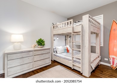 ELMHURST, IL, USA - JULY 25, 2020: A Kids Bedroom With Wooden Bunk Beds And Dresser, A Surfboard Standing In The Corner And Hardwood Flooring.