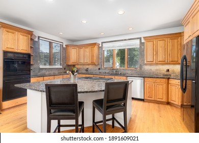 ELMHURST, IL, USA - JULY 7, 2019: A Large Luxurious Kitchen With Maple Wood Cabinets, Black Appliances, And Bar Stools Sitting At The Large Island.