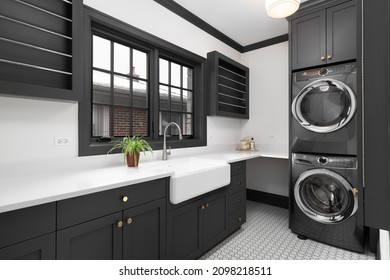 ELMHURST, IL, USA - MARCH 2, 2021: A renovated laundry room with dark grey cabinets, Electrolux appliances, farmhouse sink, and marble countertops.