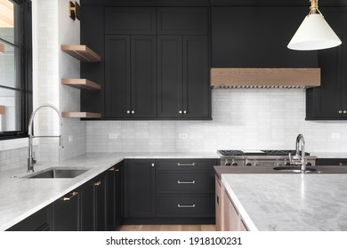 ELMHURST, IL, USA - OCTOBER 2, 2020: A Luxury Kitchen With Black Cabinets, Granite Counter Top, Tiled Backsplash, Stainless Steel Appliances, And Chrome Faucets.