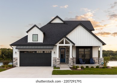 ELMHURST, IL, USA - SEPTEMBER 25, 2022: A Black And White Luxury Home With A Two Car Garage And Black Door, Professional Landscaping, And A Lake In The Background At Sunset.