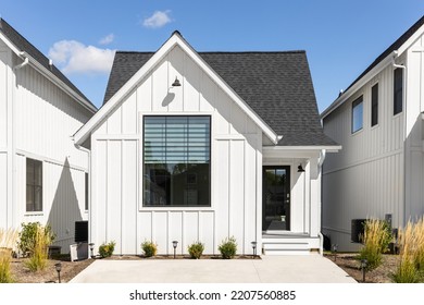 ELMHURST, IL, USA - SEPTEMBER 25, 2022: A Small, Ranch Style Modern Farmhouse With White Vertical Siding, Black Roof, Large Front Window, And Black Front Door.