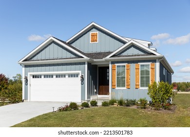 ELMHURST, IL, USA - SEPTEMBER 25, 2022: A Light Blue Ranch Home With A Two Car Garage, Wood Window Shutters,  Vertical Siding, And A Dark Wood Front Door.