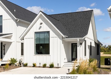 ELMHURST, IL, USA - SEPTEMBER 25, 2022: A Small, Ranch Style Modern Farmhouse With White Vertical Siding, Black Roof, Large Front Window, And Black Front Door.