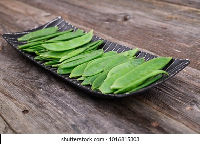 elongated bowl with green peapods  on wooden ground