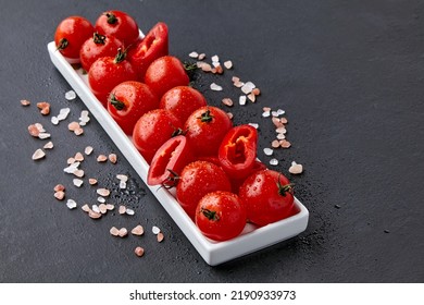 An elongated dish of tomatoes and paprika with drops of water or dew and coarse pink Tibetan salt on a black concrete table. High angle with copy space - Shutterstock ID 2190933973