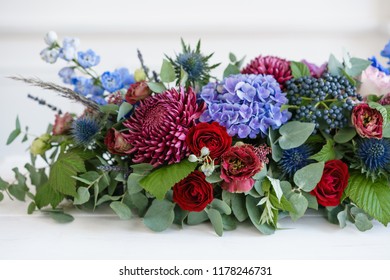 Elongated floral arrangement in vintage metal vase. table setting. Blue and red color. Gorgeous bouquet of different flowers. Bright room, stucco on the wall - Powered by Shutterstock