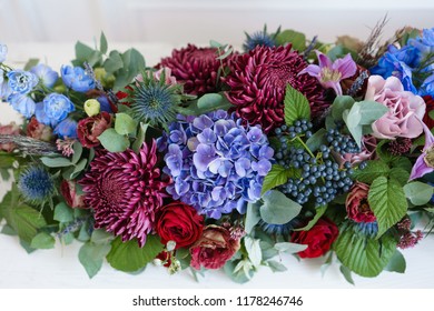 Elongated floral arrangement in vintage metal vase. table setting. Blue and red color. Gorgeous bouquet of different flowers. Bright room, stucco on the wall - Powered by Shutterstock