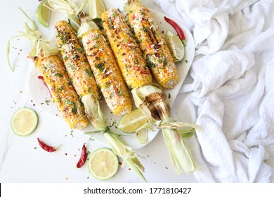 Elotes, grilled Mexican street Corn, Summer, BBQ , fast, healthy food concept, top view, flat lay, white background, decorated with red hot chili peppers lime and cilantro leaves
