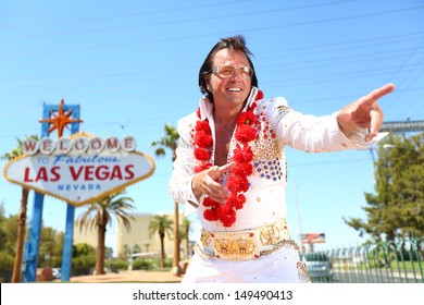 Elvis Look-alike Impersonator Man And Las Vegas Sign On The Strip. People Having Fun And Viva Las Vegas Concept Image With Elvis Impersonator Dancing Doing Some Crazy Moves Outdoor.