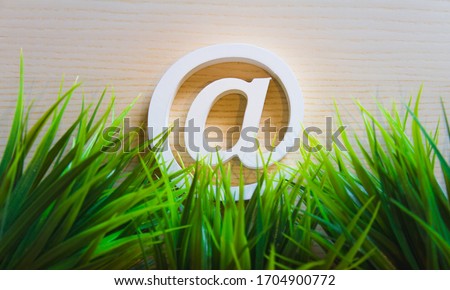 email at-sign in green grass, symbol for sustainable and environmental-friendly internet and technology, closeup with white wood atsign, top-view