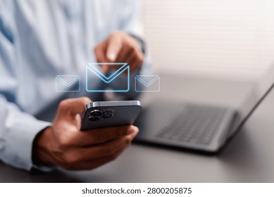 Email communication and digital message concept. Man sending mail on smartphone with envelope icons and laptop at office desk.