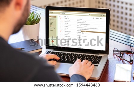 Email inbox message list on a computer laptop screen, man working on an office desk, business background. E-mail correspondence mail concept