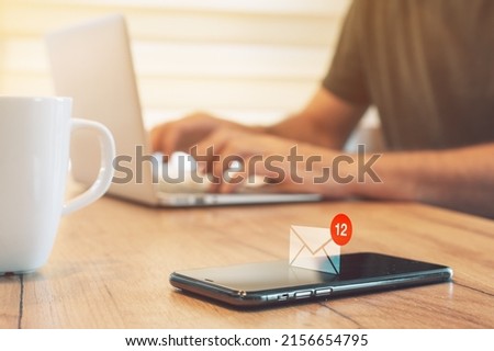 E-mail message notification pops up on mobile smart phone in home office, man typing laptop computer, selective focus
