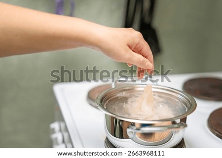 emale hand dropping raw cleaned squid into boiling water in a metal pot on an electric stove, cooking seafood at home. 