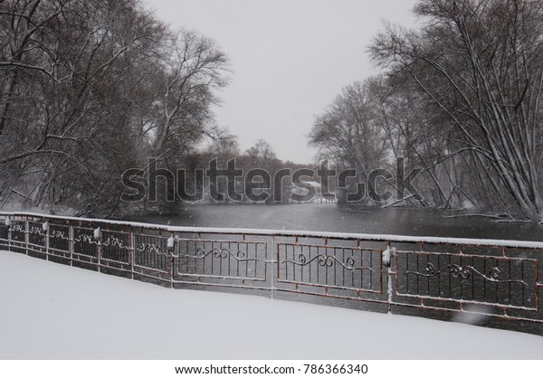 The embankment strewn with snow, with a view\
of the lake, trees, one-story houses. Outside, bad weather,\
snowstorm and snowdrifts