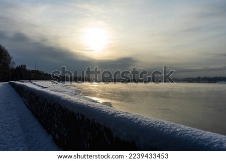 embankment in winter. Dawn on the river. Winter river in the city. City embankment by the river on a sunny winter day with snow. Falling snowflakes illuminated by the sun. Selective focus.