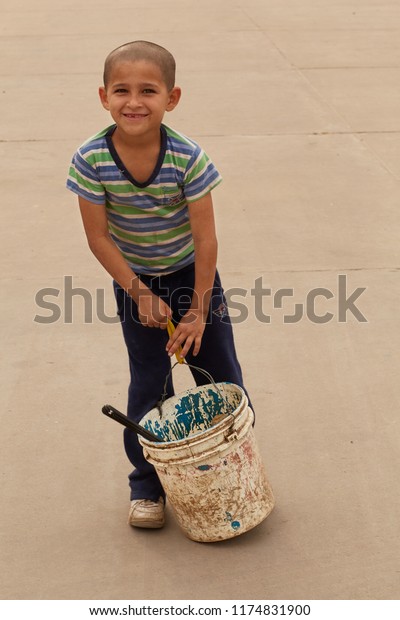 Embarcacion,\
Salta, Argentina, July 30, 2018: Candid Little Boy Washer Vehicles\
Holding a Pail With Cleaning Utensils Portrait in a Gas Station of\
Wilderness Northern Argentina Arid\
Desert