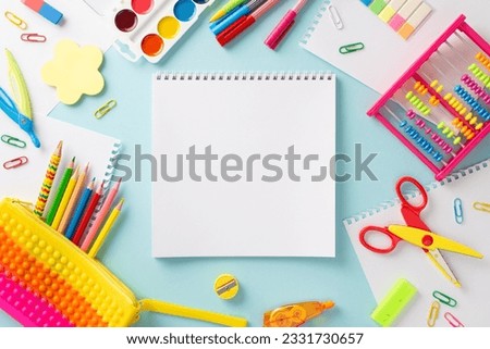 Embark on a learning adventure with this creative top view composition: colorful collection of childish school supplies on serene pastel blue surface, with blank notebook page for text or advertising