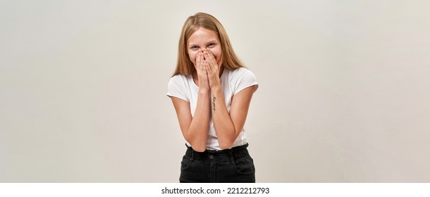 Embarrassed Caucasian Teenage Girl Covering Mouth And Looking At Camera. Female Child With Tattoo Of Zoomer Generation. Modern Youngster Lifestyle. Isolated On White Background In Studio. Copy Space