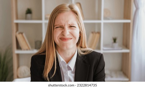 Embarrassed expression. Mistake fail. Funny confusion. Cute ashamed blond young woman in business suit with wincing grimace in light interior.
