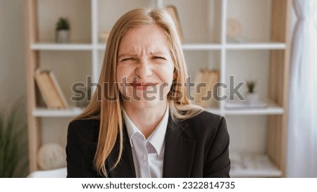 Embarrassed expression. Mistake fail. Funny confusion. Cute ashamed blond young woman in business suit with wincing grimace in light interior.
