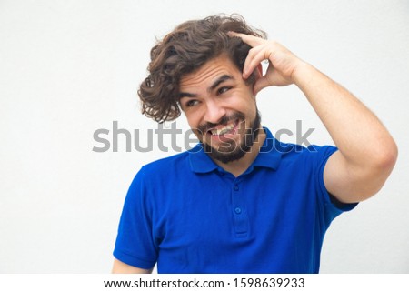 Embarrassed guilty guy scratching head, inventing excuses. Handsome bearded young man in blue casual t-shirt posing isolated over white background. Error or mistake concept