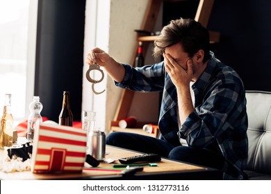 Embarrassed Man Covering Face While Holding Handcuffs After Party