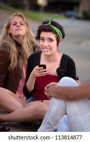 Embarrassed Teenage Girl Holding Phone Outside With Friends