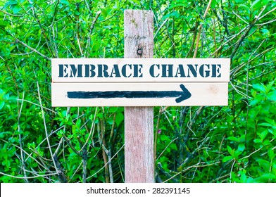 EMBRACE CHANGE written on Directional wooden sign with arrow pointing to the right against green leaves background. Concept image with available copy space