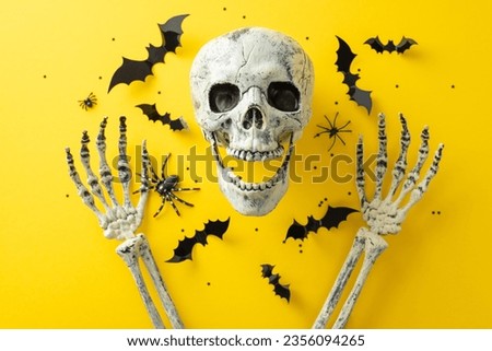 Embrace the eerie vibe of Halloween night's spookiness. Above view shot of a human skull and hands with bats and confetti on yellow isolated background, offering space for text or advertising content