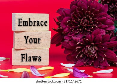 Embrace your flaws text on wooden cube and with flowers bouquet on red background.