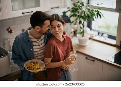 Abrazada pareja mostrando cariño mientras comía espaguetis y bebía vino en casa. 