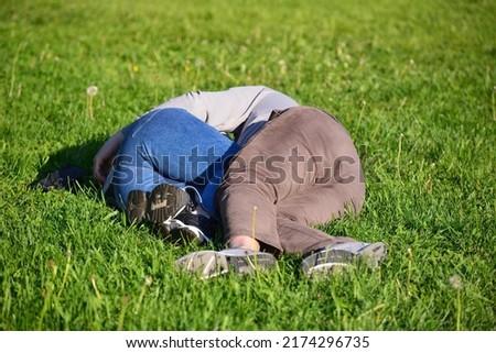 Embraced couple of a woman and man lies resting on grass of lawn in summer