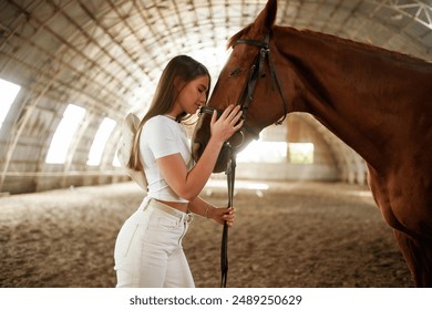 Embracing the animal. Beautiful young woman is with horse indoors. - Powered by Shutterstock