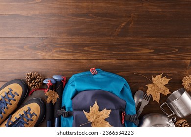Embracing autumn's charm through hiking. Top view photo of metal utensils, trekking boots, hiking backpack, trekking sticks, cones, fallen leaves on wooden background with promo spot - Shutterstock ID 2366534223