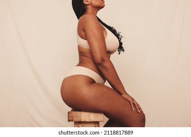 Embracing my natural curves. Body positive young woman sitting in underwear against a studio background. Self-confident young woman feeling comfortable in her natural body and curves.