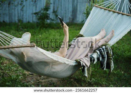Embracing Slow Living: Woman Finds Solitude in Backyard Hammock, Smartphone in Hand for a Mindful Escape