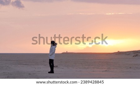 Embracing tranquility at dusk, a lone figure stands on the serene beach, captivated by the sad beauty of the sunset. The waves whisper tales of solitude as twilight paints the sky, creating a moment o