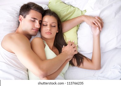 Embracing young couple sleeping on the bed