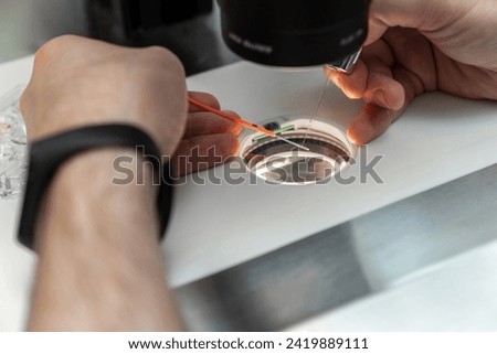 Embriologist putting sperm sample to examine under microscope or collecting in vitro cultured embryos for biopsy. Reproductive medicine clinic. Artificial insemination. Artificial conception clinic.